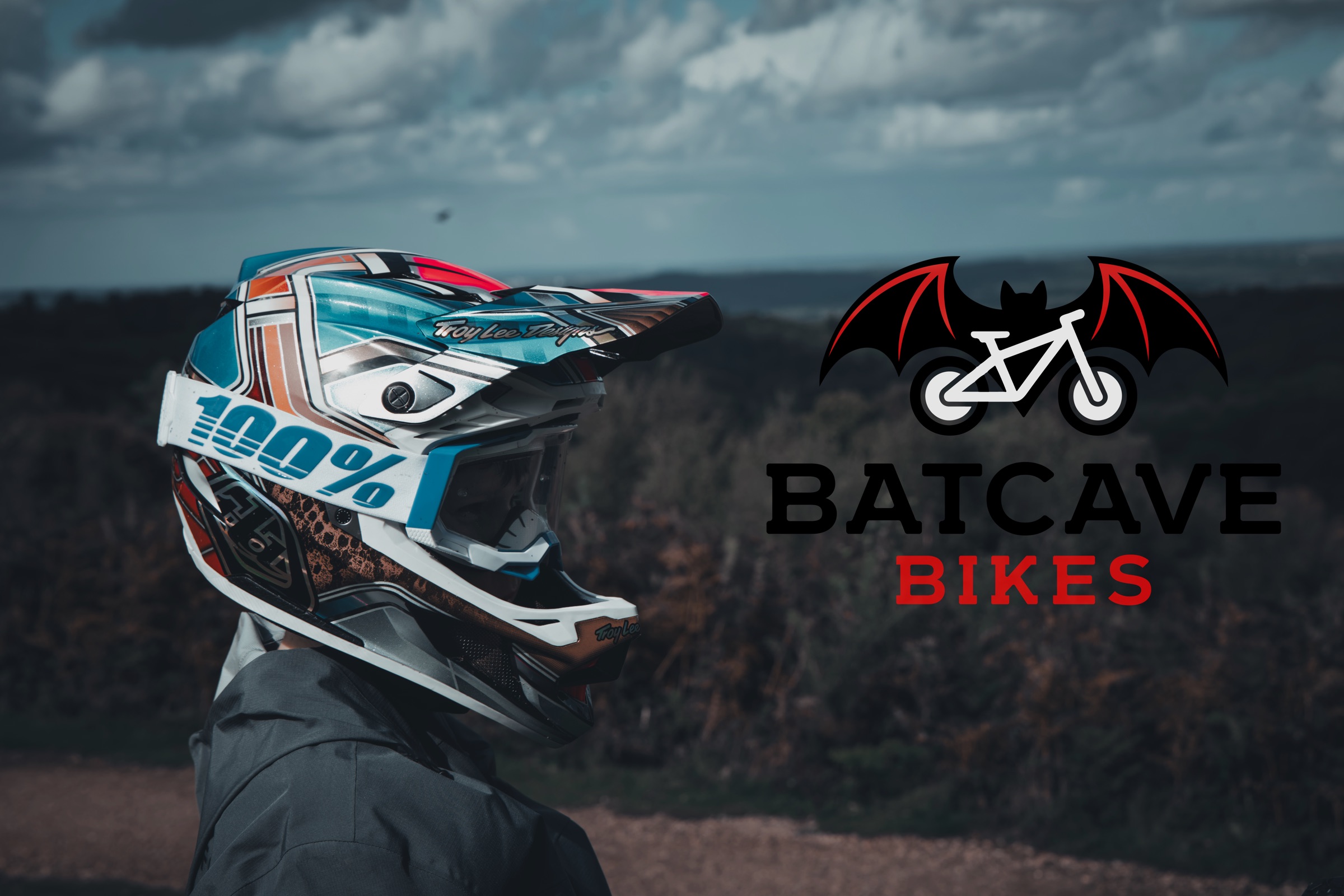 Batcave Bikes rider in a full-face helmet looking out over the hills, with the Batcave Bikes logo